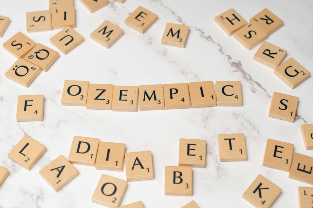 Ozempic - napis ułożony z kostek scrabble, wokół powiązane tematycznie wyrazy.