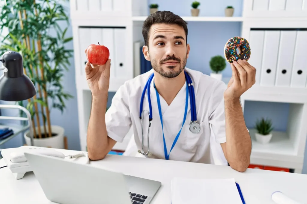 Lekarz z jabłkiem i pączkiem podczas teleporady o cholesterolu.